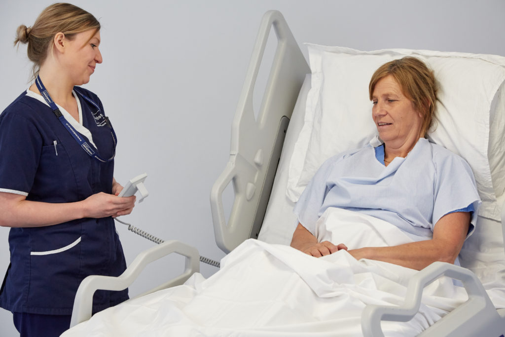 elderly patient sat in hospital bed next to standing nurse